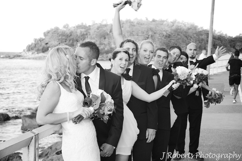 B&W bridal couple kissing and bridal party cheering - wedding photography sydney